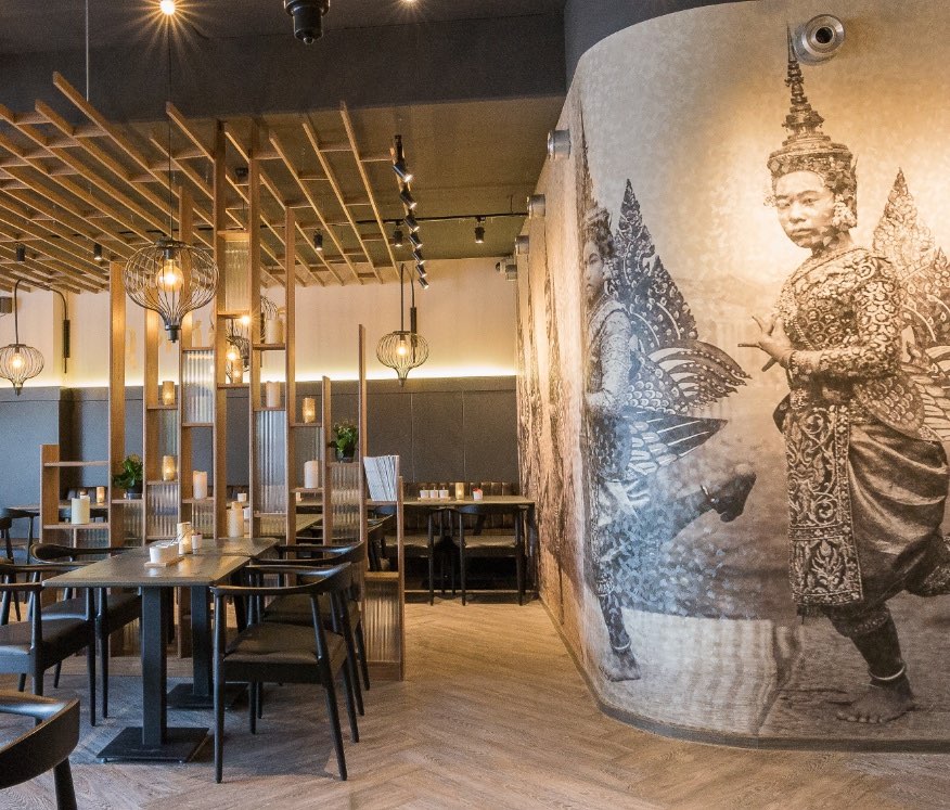 Gastraum von Station Point Thai Food mit Holzlamellen als Raumteiler und großflächigem Wandbild thailändischer Tänzerinnen